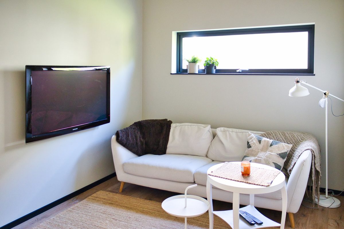 Vit soffa och väggmonterad tv i ett rum med ett högt sittande fönster