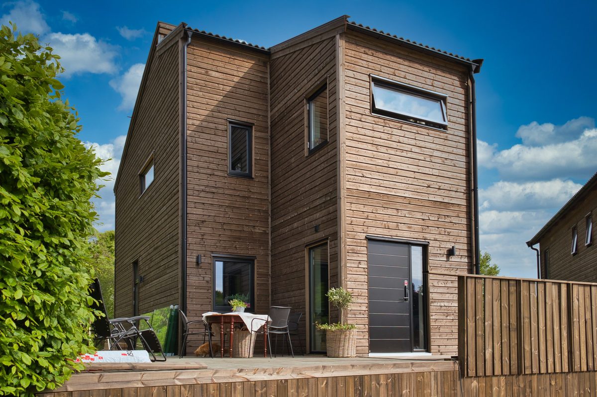 Högt trähus med brun panel och en terrass framför entrén
