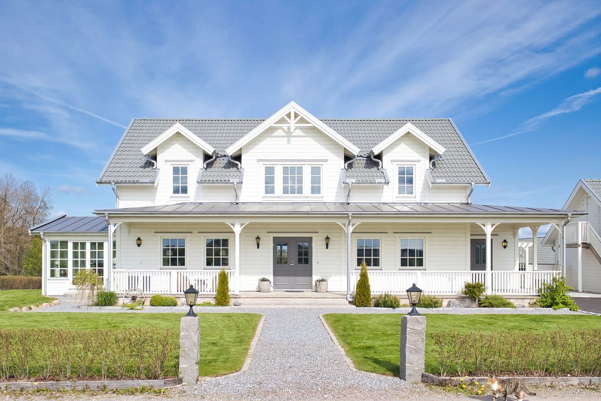 Stor vit villa i New England-stil med veranda längs fasaden, grusgång och gräsmattor framför